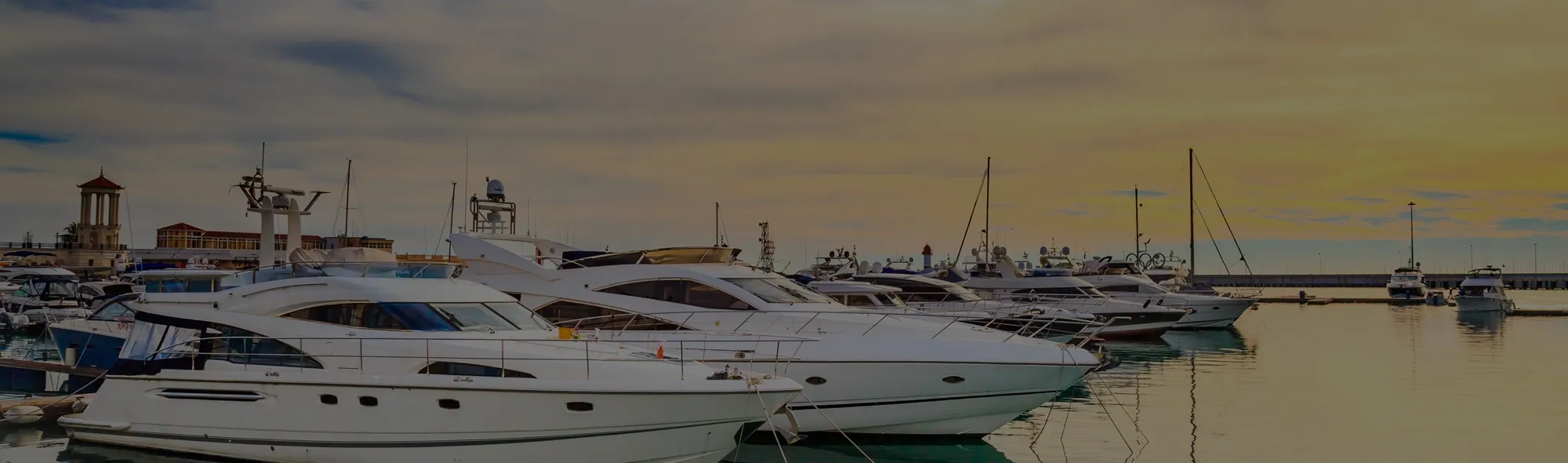 Marina filled with white luxury yachts at sunset, calm water reflecting hulls.